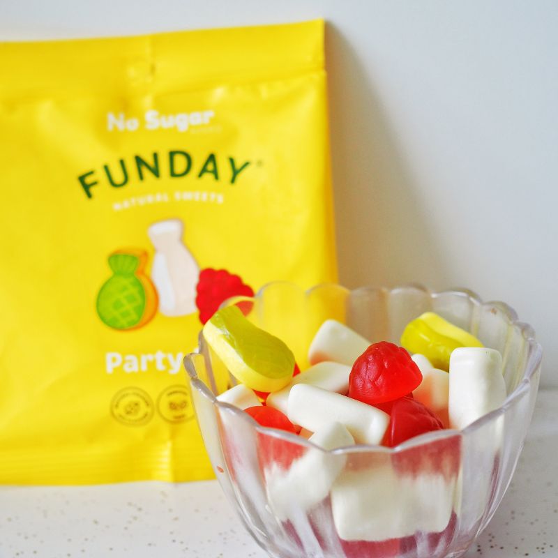 Clear glass bowl filled with red, white, and yellow gummy candies in front of a bright yellow Funday natural sweets package.