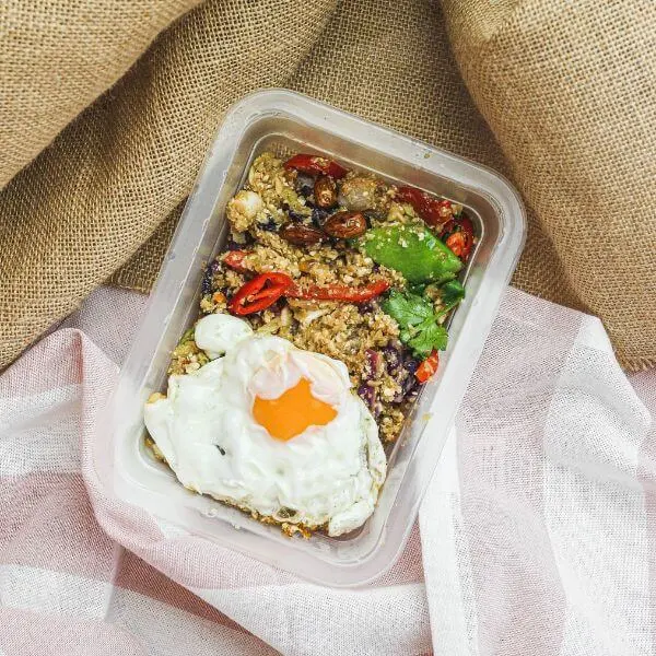 A top down photograph of a container of Nasi Goreng, topped with fried egg, nestled amongst two different cloths.